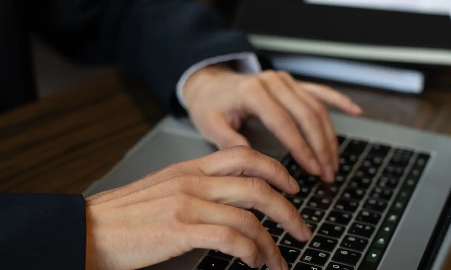 Hände auf der Tastatur eines Notebooks, im Licht eines Arbeitszimmers