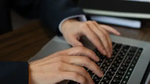 Hände auf der Tastatur eines Laptops, im Licht eines Büros