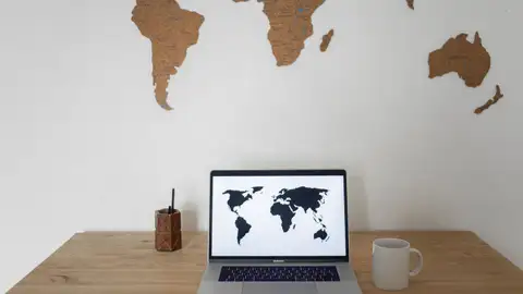 Ein Laptop zeigt eine Weltkarte, darüber eine Wandkarte